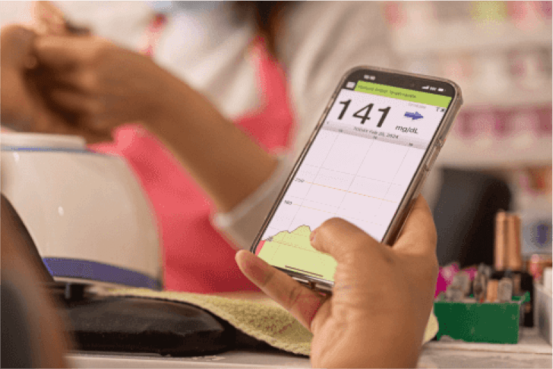 Hand holding smartphone displays "Blood Sugar: 141 mg/dL," graph, using the Eversense app